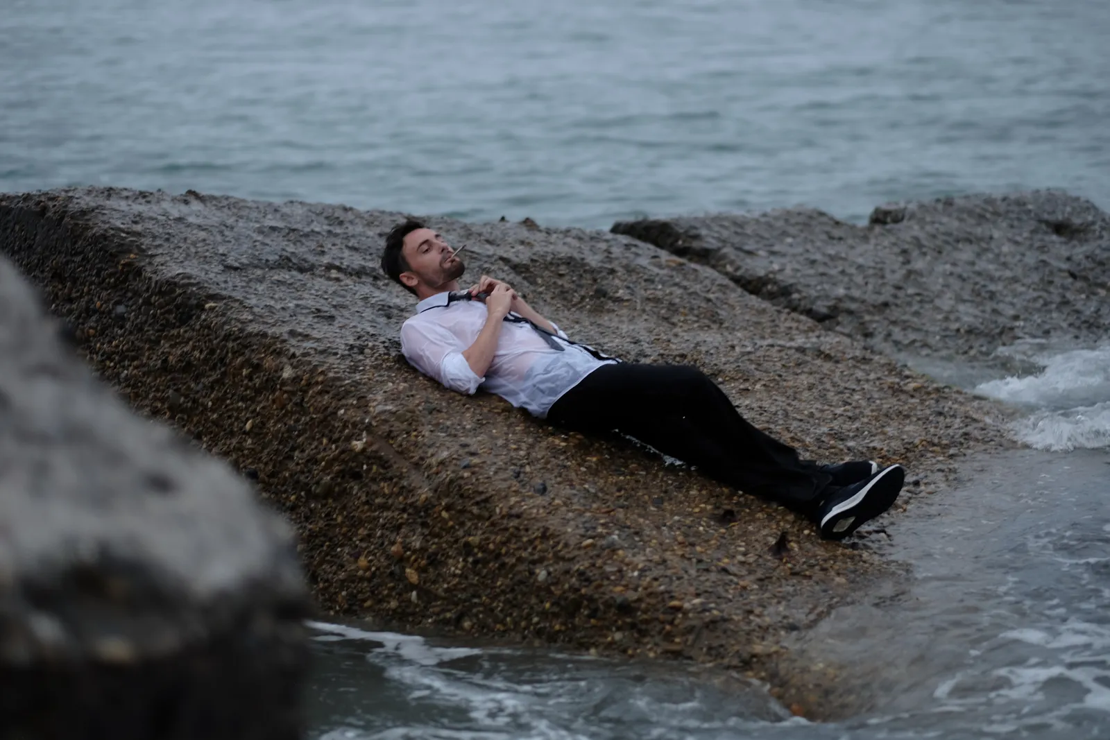 Man lying back on a rock shelf above the sea, tie across his chest