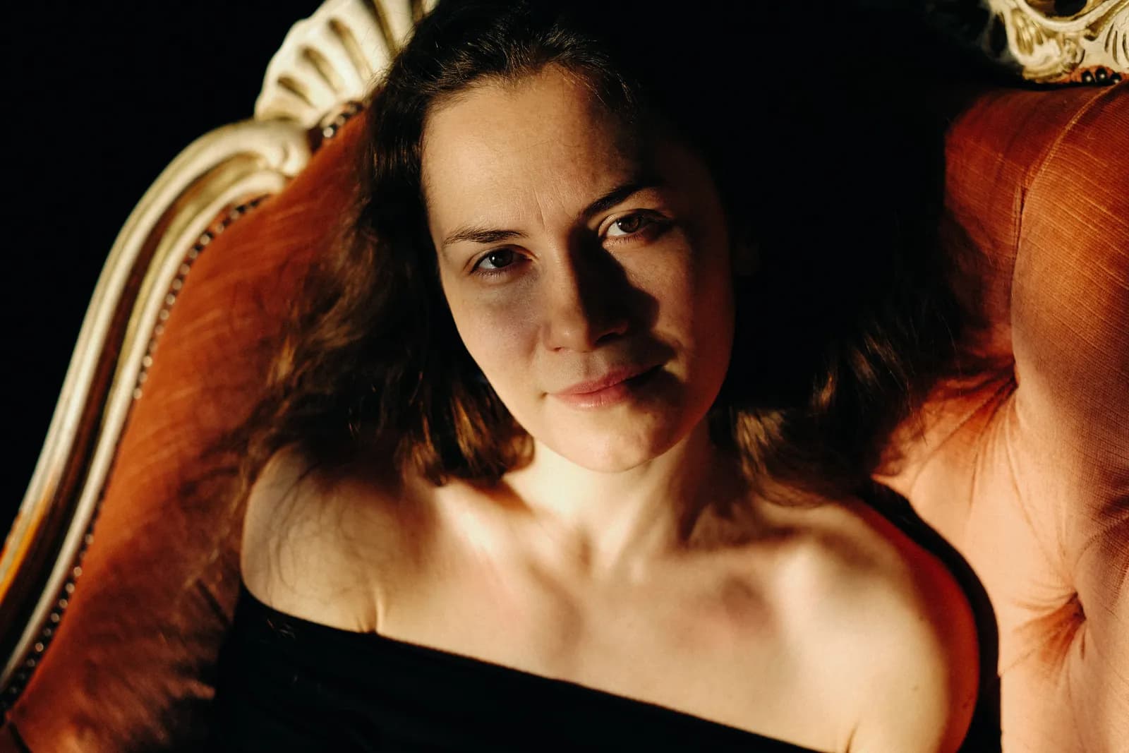 Close portrait of a woman lying back against an orange armchair, looking up into the lens